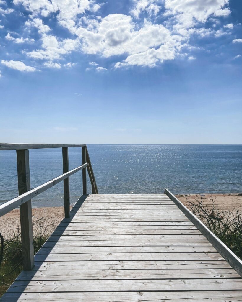 Beautiful boardwalk leading to a serene ocean view under a blue sky with fluffy clouds.
